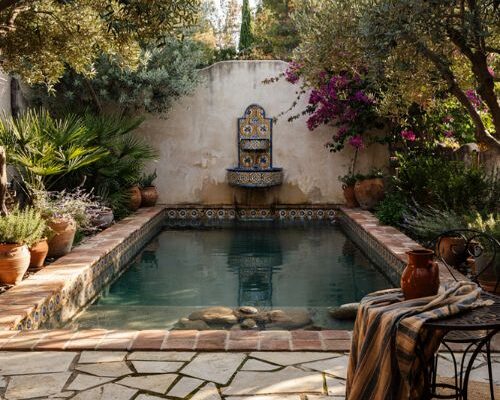 Spanish style natural pool with terracotta coping hand painted tiles and stone fountain in a garden
