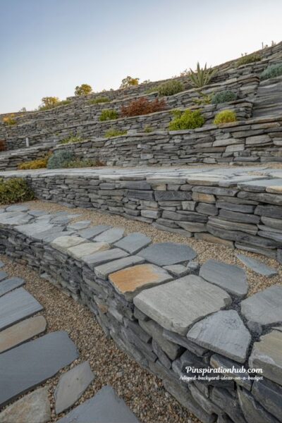 dry stacked fieldstone retaining wall terraces on sloped backyard using reclaimed stone and urbanite budget landscape design with natural drainage