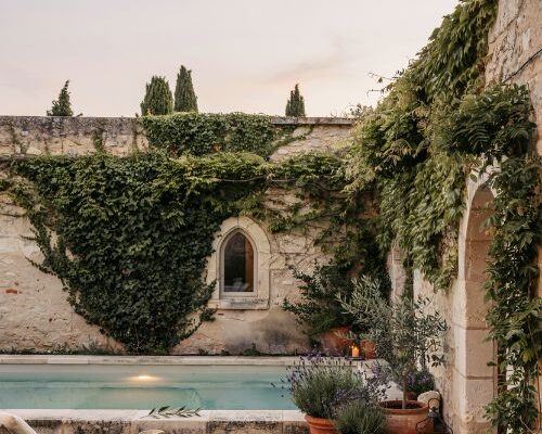 French country pool courtyard with ivy covered stone walls and glowing lanterns at dusk