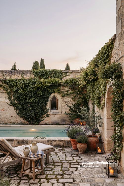 French country pool courtyard with ivy covered stone walls and glowing lanterns at dusk