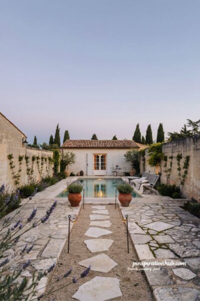 French country pool house with French doors and fairy lights pathway at twilight courtyard