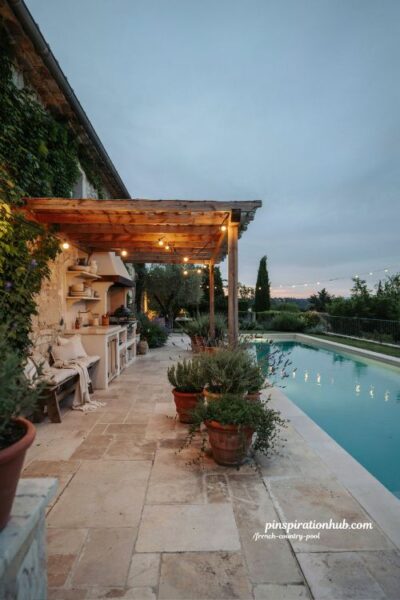 French country pool pergola with string lights and outdoor kitchen evening entertaining space