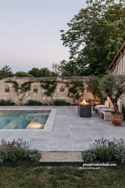 French country pool with gray stone tiles and modern fire pit evening courtyard design