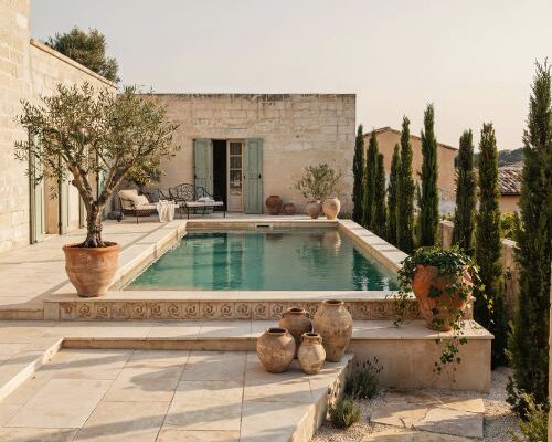 Mediterranean pool design with travertine decking and terracotta pots in a luxury European style backyard