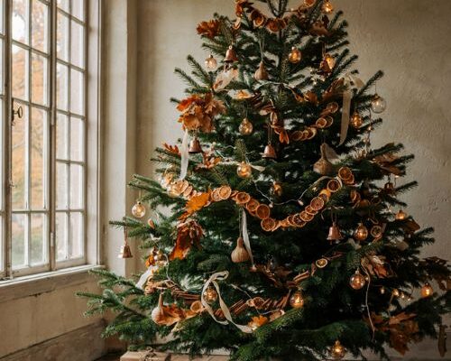 A transition christmas tree decorated with fall leaves burnt orange ribbon and copper accents in a farmhouse living room