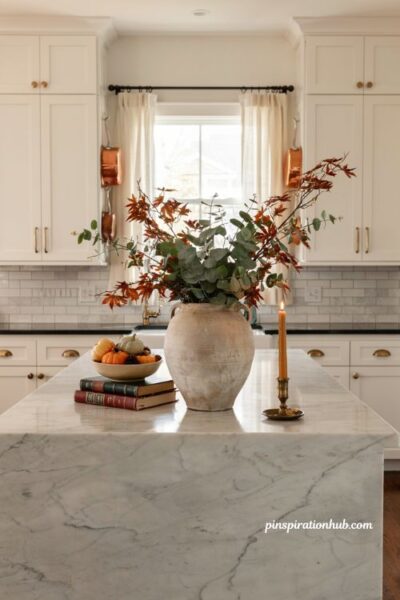 Cozy fall kitchen island decor with large ceramic vase of eucalyptus and maple leaves plus candlelight