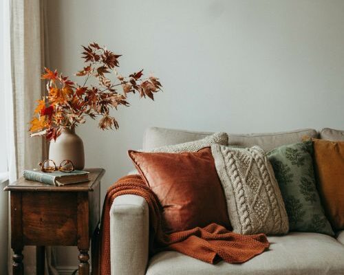 Cozy fall room decor ideas for a neutral living room with warm pillows knit throw and dried leaves