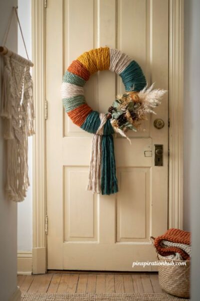 Diy yarn and floral boho wreath with tassels on a cream door for playful autumn interior decor