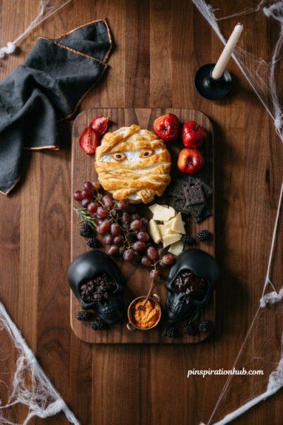 Halloween charcuterie board centerpiece with mummy pastry dark fruits and skull bowls