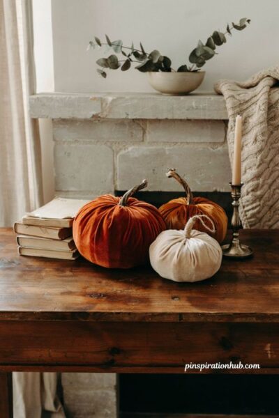Handcrafted velvet fabric pumpkins in rust orange and cream on a rustic wood console table for cozy autumn home decor.