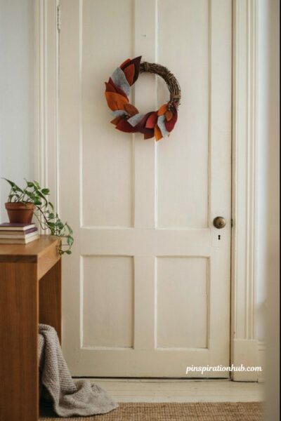 Handmade felt leaf wreath in orange red purple and gray on a white front door for cozy autumn entryway decor