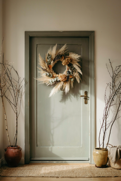 Fall wreath on weathered sage green front door with pampas grass and dried citrus for authentic autumn porch decor