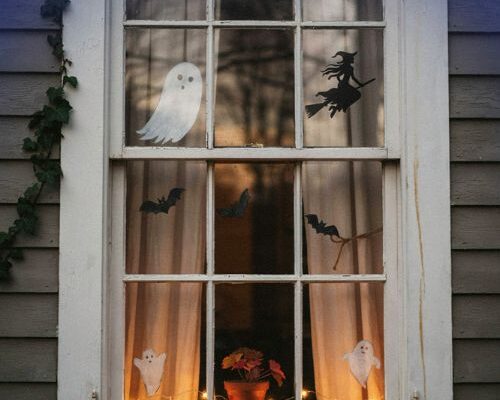 Halloween window decorations with glowing ghost, flying witch silhouette, bats and warm October window lights