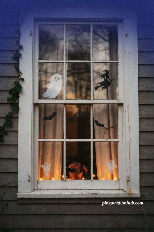 Halloween window decorations with glowing ghost, flying witch silhouette, bats and warm October window lights