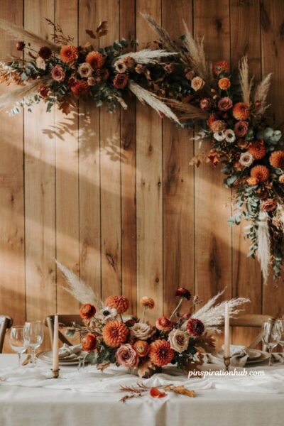 Fall wedding table decor with burnt orange floral swag natural wood backdrop and romantic autumn details